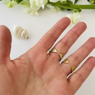 Mão segurando pequenas peças de metal dourado com concha e flores ao fundo