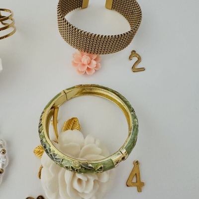 Pulseiras douradas e verde com pendentes número 2 e 4 sobre fundo branco