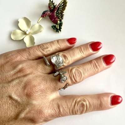 Mão com anel prateado de flor e broche de colibri colorido sobre fundo branco