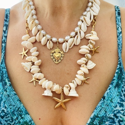 Colares com conchas, estrelas-do-mar douradas e cálices brancos, pendente dourado, sobre vestido azul com padrão abstrato