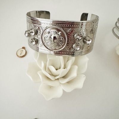 Pulseira prateada com cabeça de leão e pedras brilhantes sobre flor branca