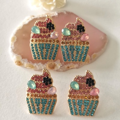 Brincos em forma de cupcake com pedras coloridas sobre suporte de pedra rosa.