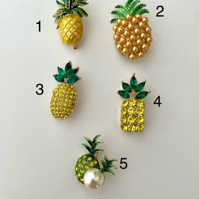 Cinco broches de ananás com pedras amarelas e verdes em fundo branco