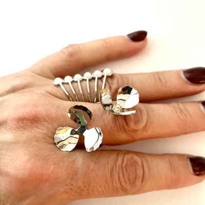 Anéis prateados de borboleta e formato de pente numa mão com unhas castanhas.