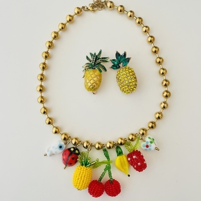 Colar dourado com pendentes coloridos de frutas e pins de ananás