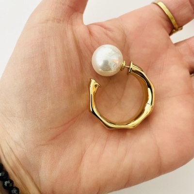 Anel dourado com pérola grande e design irregular na mão.