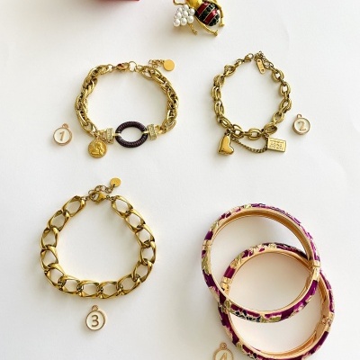 Conjuntos de pulseiras douradas e braceletes florais numerados com rosa vermelha ao fundo