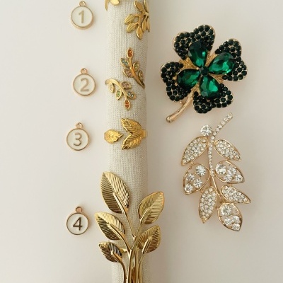 Broches dourados com pedras e desenhos de folhas, numerados de 1 a 4, sobre tecido claro.