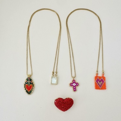 Três colares dourados com pendentes de miçangas coloridas e um coração vermelho de miçangas no centro.