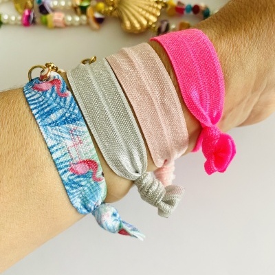 Pulseiras elásticas coloridas no pulso, com bijuteria ao fundo