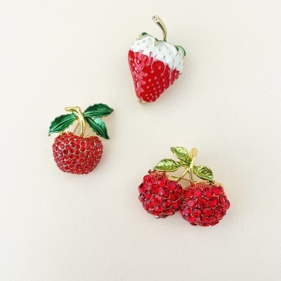 Três broches decorativos em forma de frutas vermelhas com detalhes dourados