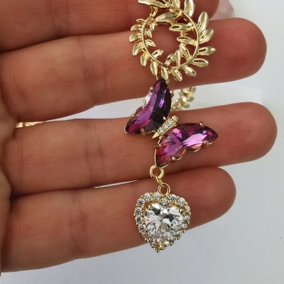 Brinco dourado com folhas, borboleta roxa e coração brilhante