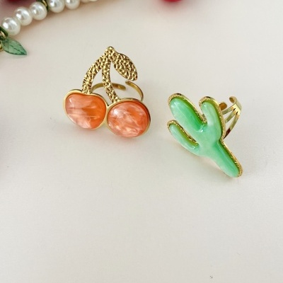 Anéis decorativos em forma de cereja laranja e cacto verde com fundo branco.