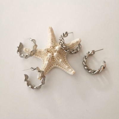 Quatro brincos de argola em metal prateado com diferentes texturas junto a uma estrela-do-mar sobre fundo branco