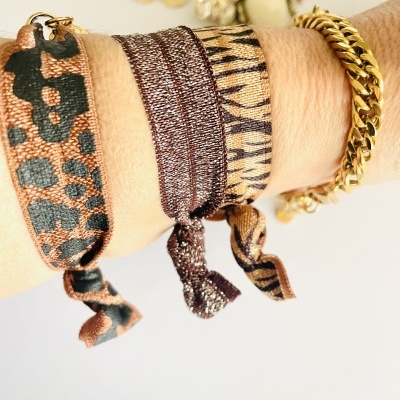 Três pulseiras de tecido com estampas animais e uma pulseira dourada de corrente no pulso