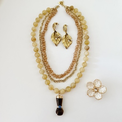 Conjunto de colar, brincos e broche em tons dourados, amarelos e castanhos sobre fundo branco