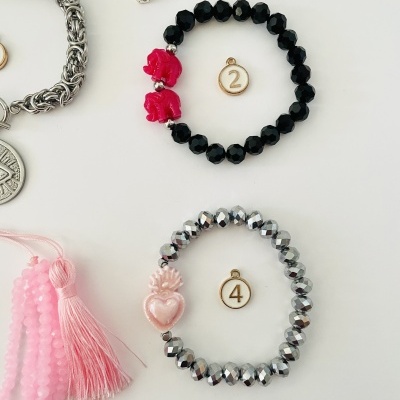 Dois conjuntos de pulseiras elásticas com contas facetadas em preto e prateado, com elementos decorativos vermelhos e rosa, e etiquetas numeradas 2 e 4