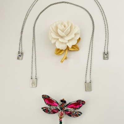 Colar com pendentes metálicos, broche flor branca com folhas douradas e joia libélula colorida