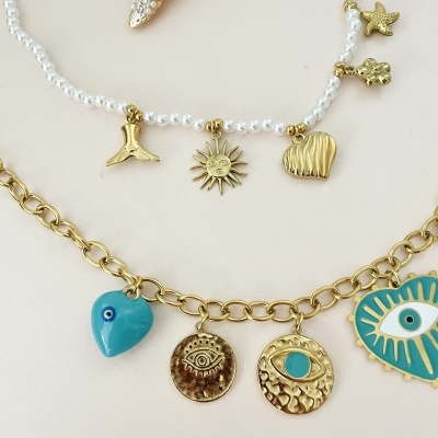 Dois colares com pendentes temáticos dourados e em azul, pendurados sobre fundo bege com estrela do mar decorativa