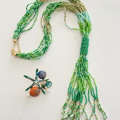 Colar de contas verde e broche com conchas e pedras coloridas sobre fundo branco