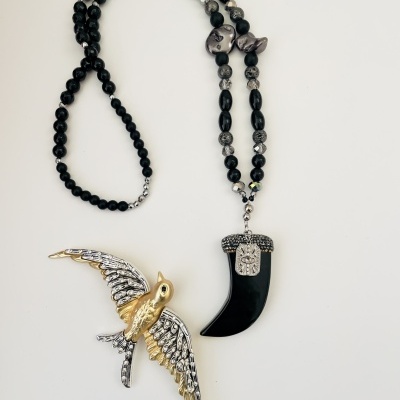 Colar preto com pendente em forma de dente e broche em forma de pássaro
