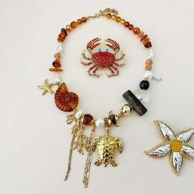 Colar com conchas e tartaruga dourada e broche de caranguejo vermelho e flor