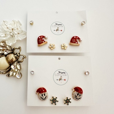 Brincos natalícios com gorros de Pai Natal, flocos de neve e pedras prateadas em cartão branco.