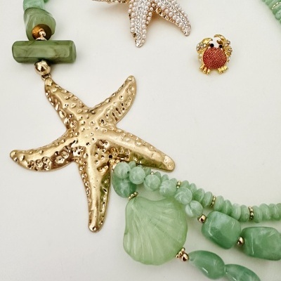 Colar com contas verdes e pendentes em forma de estrela do mar e caranguejo sobre fundo branco