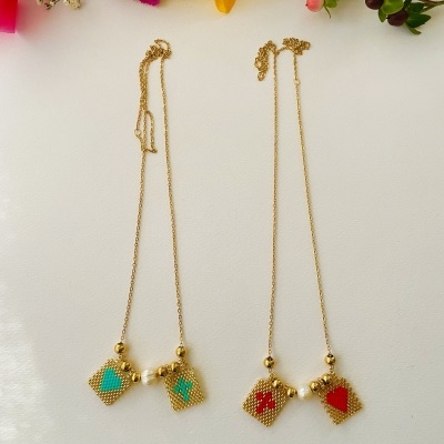 Dois colares dourados com pingentes quadrados coloridos ao lado de flores coloridas