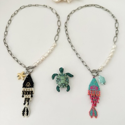 Dois colares com pérolas e pendentes de peixe feitos de contas, broche de tartaruga verde, fundo branco