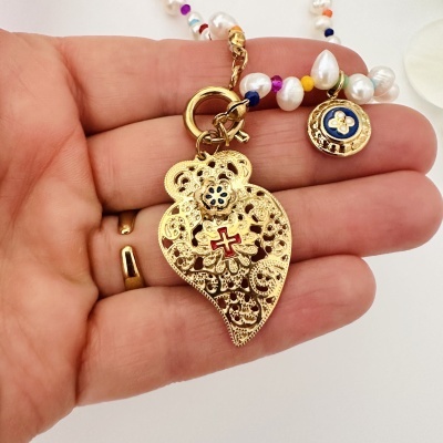 Colar dourado com pendente em forma de coração e contas coloridas, segurado na mão
