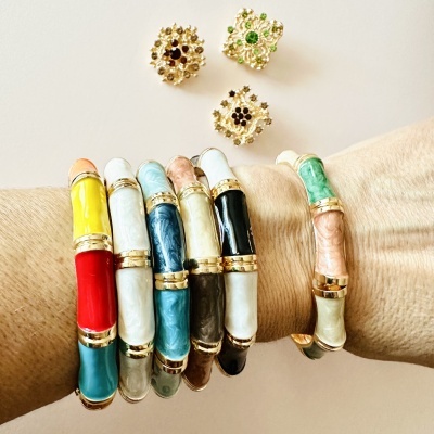 Pulseiras coloridas esmaltadas com detalhes dourados num pulso e botões dourados ao fundo