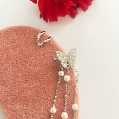 Brincos em metal com pedras brilhantes e pérolas sobre tecido rosa com flor vermelha ao fundo