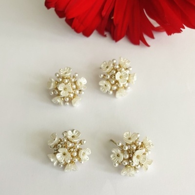 Brincos cluster com pérolas e flores bege em fundo branco e flor vermelha próxima.