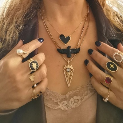 Pessoa a usar colares dourados com pingentes pretos e vários anéis diversos com pedras e pérola