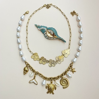 Colares com pérolas e pendentes dourados junto a um broche azul com pérolas e detalhes dourados