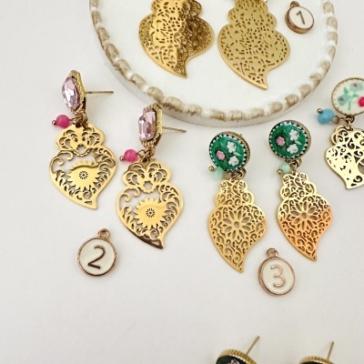 Brincos dourados ornamentados com pedrarias e pintura floral, com etiquetas numeradas.