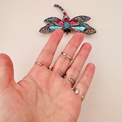 Mão com anéis prateados e dourados segurando borboleta decorativa colorida