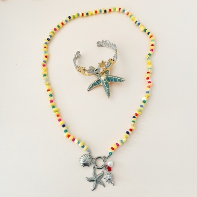 Colar colorido com contas pequenas e pendentes marinhos com anel prateado com estrela-do-mar azul, sobre fundo branco.