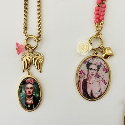 Colares com pendentes ovais dourados com imagens da pintora Frida Kahlo e contas cor-de-rosa sobre fundo branco.
