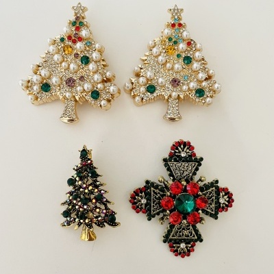 Quatro broches natalícios com pérolas e pedras coloridas sobre fundo branco