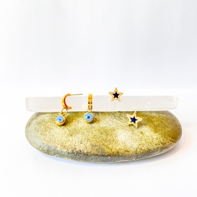 Brincos dourados com olho turco azul e branco e brincos de estrela azul escuro sobre pedra cinzenta e cristal