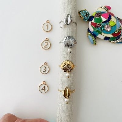 Anéis com pérolas penduradas em suporte de tecido com plaquinhas numeradas e broche de tartaruga colorida