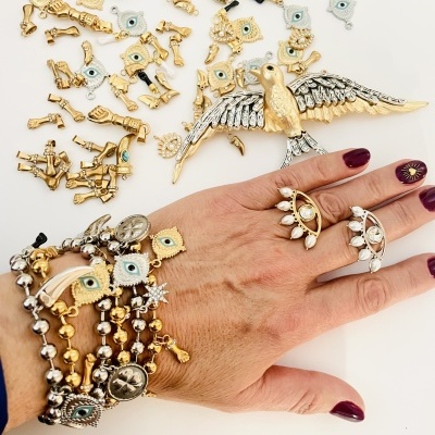 Mão com anéis e pulseiras de contas douradas e prateadas com amuletos vários sobre fundo branco