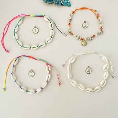 Quatro pulseiras numeradas com conchas e contas, e um broche azul decorativo sobre fundo claro
