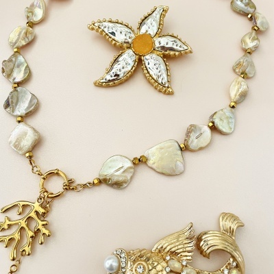Colar de madrepérola com pingentes dourados e broche de flor dourada com centro laranja