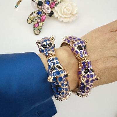 Braceletes de cabeça de pantera dourada com esmalte azul e roxo no pulso e broche de flor branca ao fundo