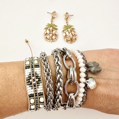 Pulseiras variadas em pulso e brincos de abacaxi com pedras douradas e verdes