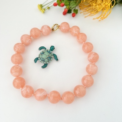 Colar coral com pendente de tartaruga verde e azul sobre fundo branco com flores