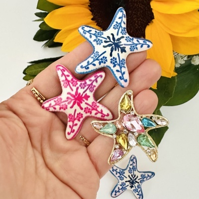 Brincos de estrela do mar em cerâmica branca azul e rosa e dourado com cristais coloridos em mão com girassol ao fundo